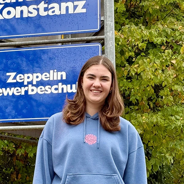 Person im blauen Hoodie vor Schildern.