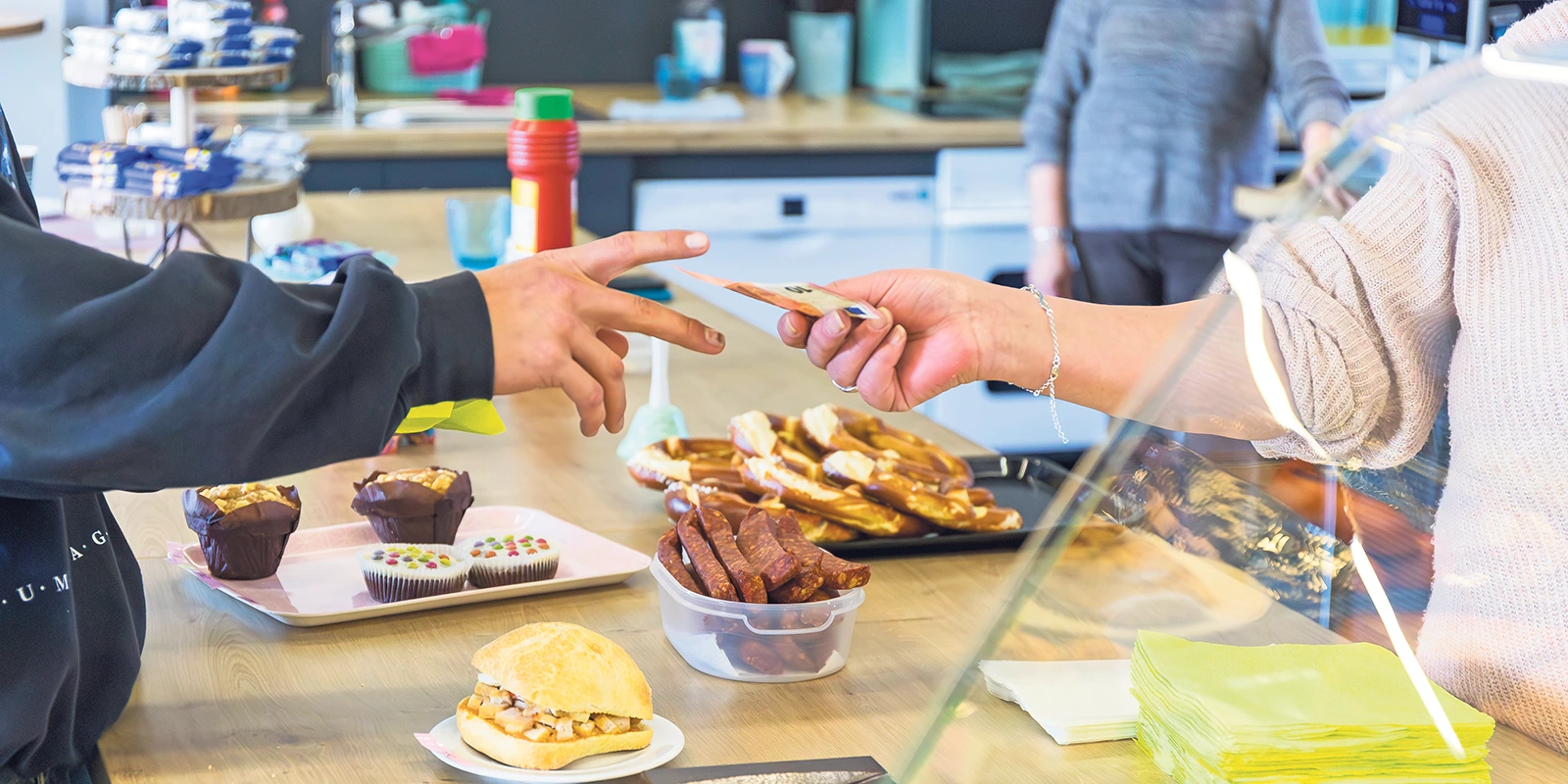 Hände überreichen Geld für Backwaren.